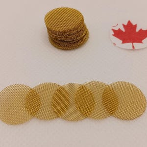 May include: Six gold-colored metal mesh screens, each about 2 inches in diameter, are arranged in a row. A stack of similar screens is in the background.