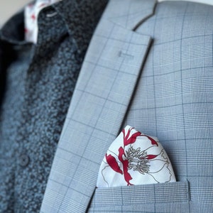 Puede incluir: Una chaqueta de traje gris a cuadros con un pañuelo de bolsillo blanco con un diseño floral rojo.