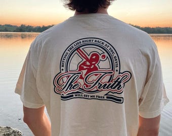 May include: A white t-shirt with a red and blue graphic on the back. The graphic features a baseball bat and ball with the text "The Truth Will Set Me Free" and "Hitting the Lies Right Back at You, Devil".