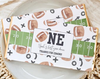 May include: A white chocolate bar with a football theme. The wrapper features a brown football pattern, green and white yard lines, and the text "ONE Noah's first year down THANKS FOR COMING!"