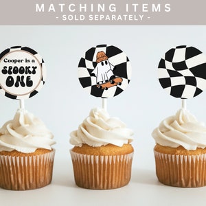 K&ouml;nnte beinhalten: Drei Cupcakes mit wei&szlig;em Frosting und schwarz-wei&szlig;en karierten Cupcake-Toppern. Ein Topper sagt "Cooper is a spooky one" und hat ein schwarz-wei&szlig;es Karomuster. Ein weiterer Topper zeigt ein Gespenst mit M&uuml;tze, das auf einem Skateboard f&auml;hrt. Der dritte Topper ist ein schwarz-wei&szlig;es Karomuster.