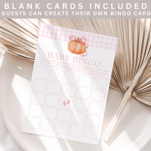 May include: A Baby Bingo card with a pumpkin illustration and pink gingham pattern. The card includes blank spaces for guests to fill in. The text "Baby Bingo" is at the top of the card.