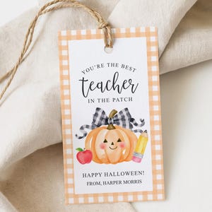 May include: A rectangular gift tag with a light orange gingham border, featuring a watercolor pumpkin with a black and white plaid bow, a red apple, and a yellow pencil. Text reads: YOU'RE THE BEST teacher IN THE PATCH HAPPY HALLOWEEN! FROM, HARPER MORRIS.