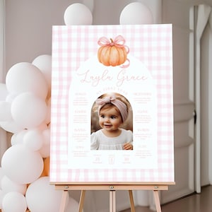Puede incluir: Un letrero rosa y blanco con estampado de cuadros vichy sobre un caballete, con una foto de una niña. El letrero incluye el texto "Layla Grace My First Year" con una ilustración de calabaza y detalles sobre el primer año del bebé, incluido el peso en libras.
