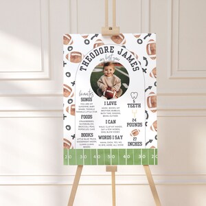 May include: A white and green football-themed growth chart with a photo of a baby boy. The chart lists the baby's name, Theodore James, and includes details like his age, weight, height, favorite songs, foods, and books. The chart is decorated with brown footballs and green and white stripes.
