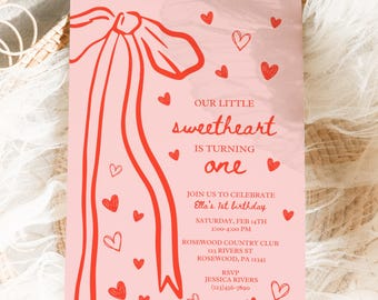 May include: Pink and red birthday invitation featuring a red ribbon bow and hearts. The text reads "Our Little Sweetheart is Turning One." The invitation includes the date, time, location, and RSVP information.