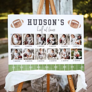 Puede incluir: Un letrero blanco sobre un caballete de madera con el texto "HUDSON'S hall of fame" e im&aacute;genes de un beb&eacute; con un bal&oacute;n de f&uacute;tbol para cada mes de su primer a&ntilde;o. El letrero tiene un dise&ntilde;o de campo de f&uacute;tbol en la parte inferior.