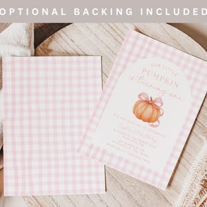 May include: Two pink gingham-patterned invitation cards with the text "Our Little Pumpkin is turning one" and a pumpkin illustration. The cards are on a wooden surface with decorative elements.