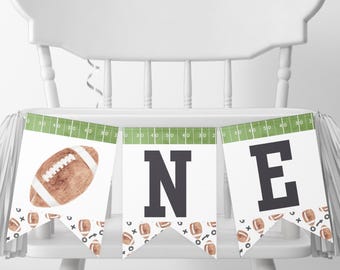 May include: A white high chair with a green and white football-themed banner that says "ONE". The banner has brown footballs and green and white football field graphics.