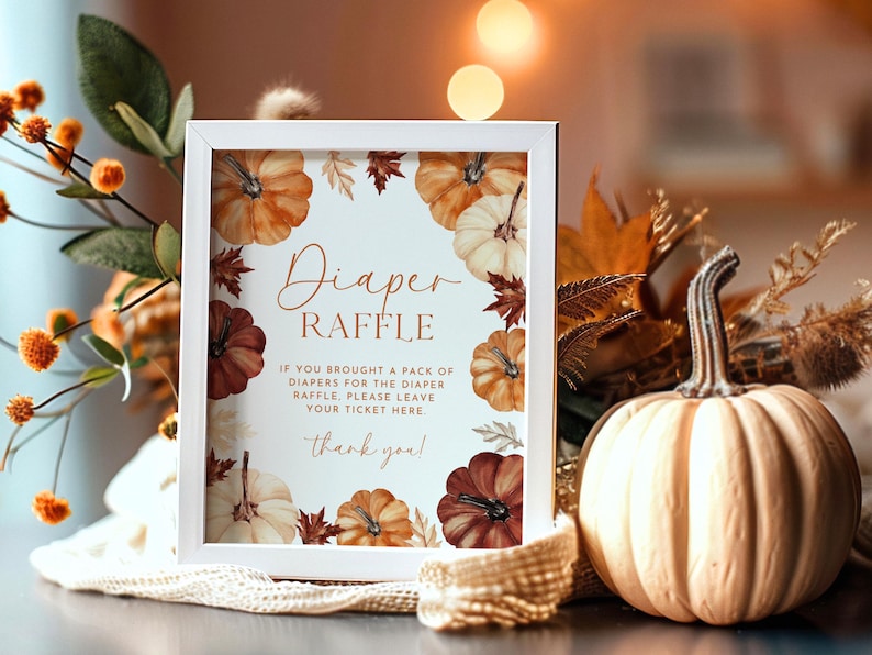 May include: A white framed sign with the words "Diaper Raffle" surrounded by watercolor pumpkins and fall leaves. A decorative pumpkin and fall foliage are in the background. The sign reads "If you brought a pack of diapers for the diaper raffle, please leave your ticket here. Thank you!"