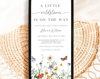 May include: A white phone screen with a baby shower invitation. The invitation has a floral design with the text "A Little Wildflower Is On The Way" and details for the event, including the name "Hanna Nelson", date, time, location, RSVP information, and registry details.