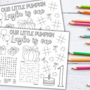 Puede incluir: Dos p&aacute;ginas para colorear en blanco y negro con el texto "OUR LITTLE PUMPKIN Layla is one". Las p&aacute;ginas presentan globos, regalos, calabazas, cuadr&iacute;culas de tres en raya, lazos, un laberinto, una tarta y el n&uacute;mero 1. L&aacute;pices de colores visibles a la derecha.