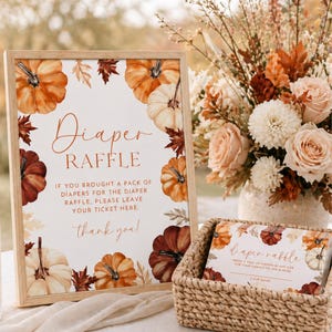 May include: A wooden framed sign with the words "Diaper Raffle" and pumpkin illustrations. The sign includes text that reads "If you brought a pack of diapers for the diaper raffle, please leave your ticket here." A basket with raffle tickets is in front.