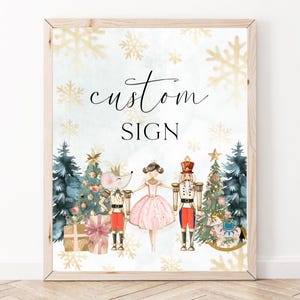 Könnte beinhalten: Ein weißes Schild mit dem Text "custom sign" in schwarzer Schreibschrift. Das Schild zeigt eine Aquarell-Illustration eines Nussknackers, einer Ballerina und einer Maus vor einem Weihnachtsbaum. Der Hintergrund ist hellblau mit goldenen Schneeflocken.