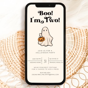 May include: A smartphone screen displaying a Halloween party invitation with a ghost holding a jack-o-lantern. The invitation reads "Boo! I'm Two!" and includes the party details: "Join us for a Halloween Party, 4:00-7:00 PM, Addams Home, 123 State St., Transylvania, PA. Wear your best costume for a chance to win a prize. RSVP Melinda (123)456-7890 | Melsmith@email.com"