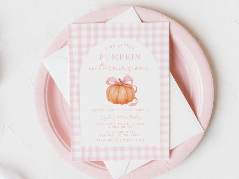 May include: A pink and white gingham-patterned invitation card with the text "Our Little Pumpkin is turning one." The card features a watercolor pumpkin with a pink bow. The invitation is on a pink plate with a white envelope.