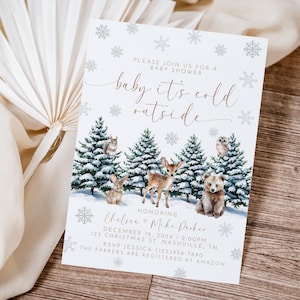 Puede incluir: Una invitaci&oacute;n de baby shower blanca con un tema de invierno. La invitaci&oacute;n presenta una escena de bosque nevado con animales, incluyendo un ciervo, un oso y una ardilla. El texto de la invitaci&oacute;n dice "baby it's cold outside" e incluye los nombres Chelsea y Mike Parker, la fecha y la hora de la ducha, y la direcci&oacute;n.