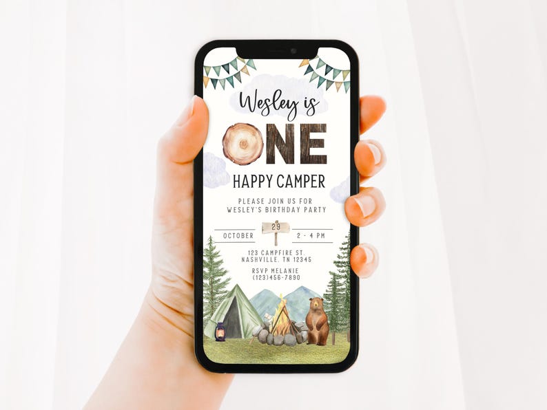 May include: A digital invitation for a first birthday party with a woodland camping theme. The invitation features a brown wooden number one, a bear, a campfire, and a tent. The text on the invitation reads "Wesley is One Happy Camper".