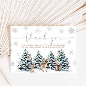 Puede incluir: Tarjeta de agradecimiento con un tema de bosque invernal. La tarjeta presenta una escena de bosque nevado con un ciervo, un oso, un b&uacute;ho y un conejo. El texto en la tarjeta dice: "&iexcl;Gracias por colmarnos de amor y por compartir la celebraci&oacute;n de nuestro peque&ntilde;o tesoro!"