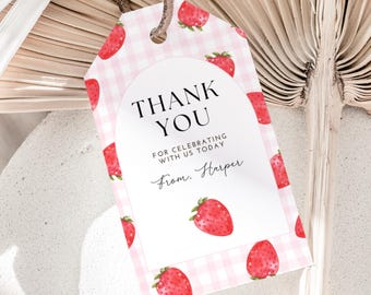 Puede incluir: Una etiqueta rosa y blanca a cuadros con un diseño de fresas y las palabras "THANK YOU" en negro. La etiqueta incluye el texto "FOR CELEBRATING WITH US TODAY" y "From. Harper". Una cuerda marrón está adjunta.