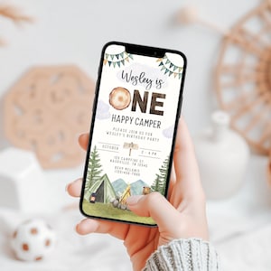 May include: A digital invitation for a first birthday party with a woodland camping theme. The invitation features a wood-grain background with the text "Wesley is ONE" and "Happy Camper". The invitation also includes details about the party, such as the date, time, and location.
