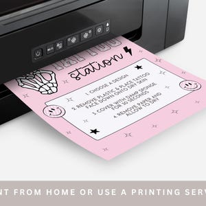 May include: A pink sheet with temporary tattoo instructions emerges from a black printer. The sheet features the word "station" and steps for application. The instructions include choosing a design, removing plastic, and allowing the tattoo to dry.