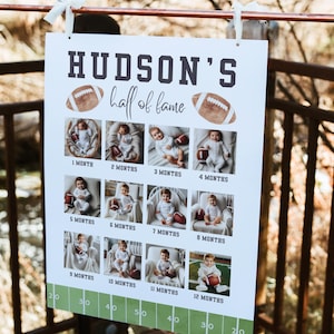 Puede incluir: Un letrero blanco con el texto "HUDSON'S half of fame" e ilustraciones de f&uacute;tbol. Presenta una cuadr&iacute;cula de fotos de beb&eacute;s de 1 a 12 meses, cada uno sosteniendo un bal&oacute;n de f&uacute;tbol. La parte inferior tiene un dise&ntilde;o de campo de f&uacute;tbol verde.