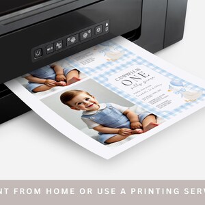 May include: A black printer printing a baby's first birthday invitation. The invitation features a photo of a baby in blue overalls, with text that reads "Campbell is One". The background has a blue gingham pattern.