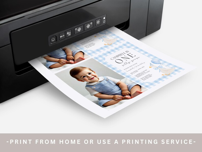 May include: A black printer printing a baby's first birthday invitation. The invitation features a photo of a baby in blue overalls, with text that reads "Campbell is One". The background has a blue gingham pattern.
