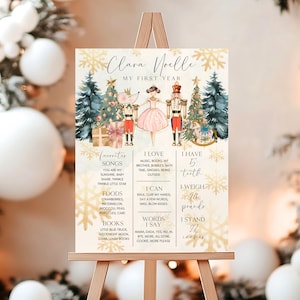 May include: A gold and white printable first birthday milestone poster featuring a Nutcracker and a ballerina with a mouse. The poster includes the child's name, Clara Noelle, and details about their first year, including favorite songs, foods, books, and milestones like weight and height.