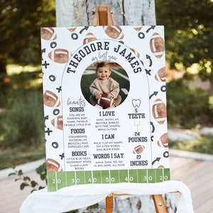 May include: A white and green football-themed first birthday milestone poster with a photo of a baby boy. The poster includes the baby's name, Theodore James, and details about his first year, including his favorite songs, foods, and books. The poster also includes his height, weight, and number of teeth.