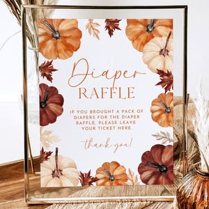 May include: A framed sign with a fall theme. The sign reads "Diaper Raffle" with watercolor pumpkins and leaves. The text below explains the raffle rules and includes a "thank you" message.