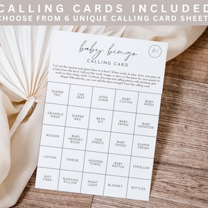 May include: A white baby bingo calling card with a grid of baby-related items, including "Diaper Pail" and "Stroller." The card is on a wooden surface, with text at the top that reads "CALLING CARDS INCLUDED."