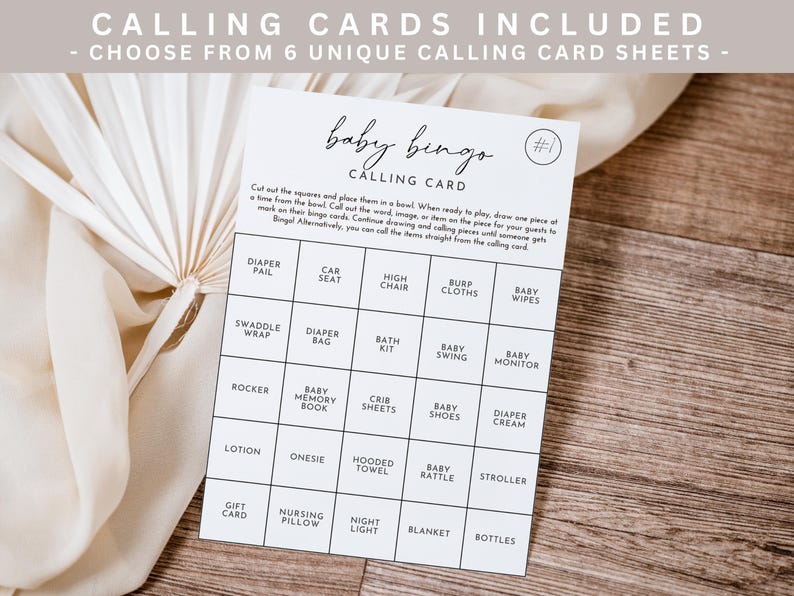 May include: A white baby bingo calling card with a grid of baby-related items, including "Diaper Pail" and "Stroller." The card is on a wooden surface, with text at the top that reads "CALLING CARDS INCLUDED."
