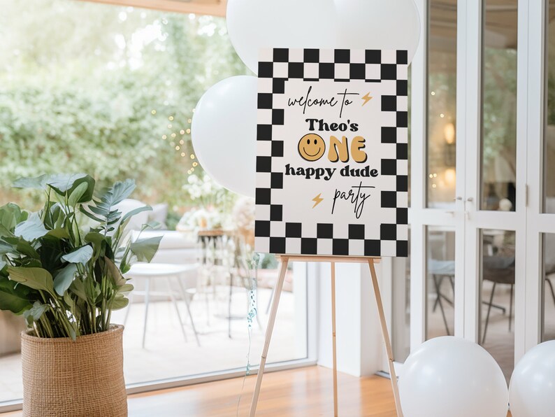 Puede incluir: Un cartel de bienvenida a cuadros blanco y negro con el texto "Bienvenido a la fiesta de Theo's One happy dude" en letras doradas y blancas. Se incluye una carita sonriente en el texto.