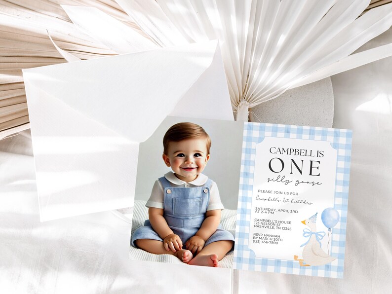 May include: A baby boy in a blue romper smiles next to a birthday invitation. The invitation has a blue gingham border and features a cartoon goose holding a balloon. The text reads "Campbell is One silly goose."