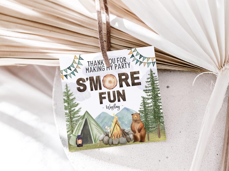 May include: A white thank you tag with a brown bear, a campfire, and a tent. The text reads "Thank you for making my party s'more fun - Wesley".