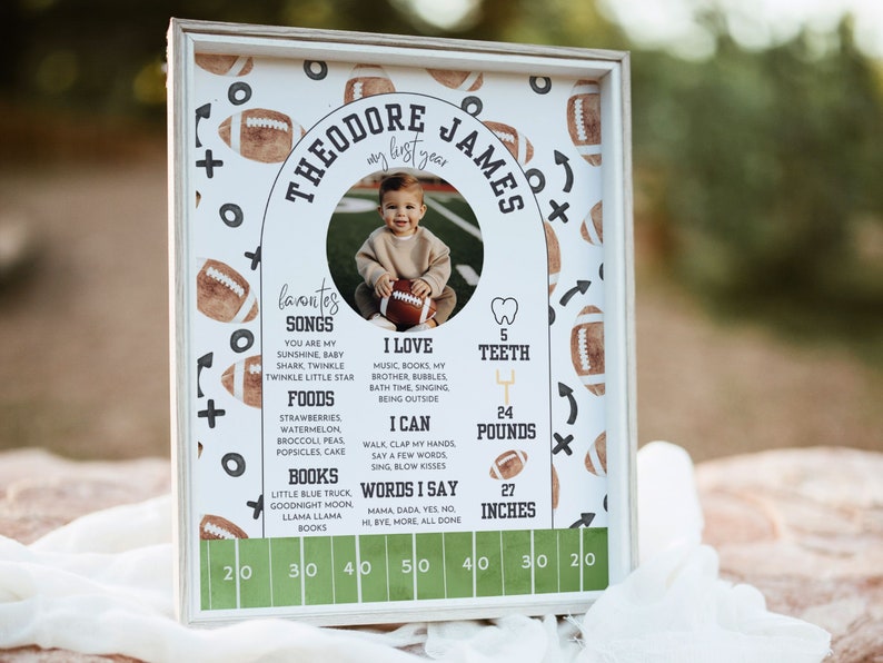 May include: A white framed print with a football theme. The print features a photo of a baby boy, along with a list of his favorite songs, foods, books, and things he can do. The print also includes his age, weight, and height. The text on the print reads "Theodore James, my first year".