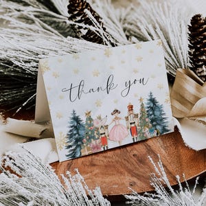 May include: A folded thank you card with a winter holiday theme. The card features a watercolor illustration of a ballerina, nutcracker, and mouse king. The words "Thank you" are written in elegant script.