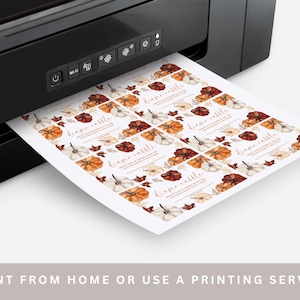 May include: A black printer is printing a sheet of paper with fall-themed diaper raffle cards. The cards feature watercolor pumpkins in shades of orange, white, and brown, with fall leaves. The text "diaper raffle" is visible on each card.