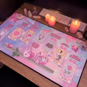 Puede incluir: Una alfombrilla de escritorio rectangular con un fondo de galaxia en tonos rosa y azul pastel, que presenta ilustraciones de cartas del tarot como La Emperatriz, Los Enamorados, La Sacerdotisa, La Estrella, El Sol y La Luna, junto a motivos de corazones y flores.