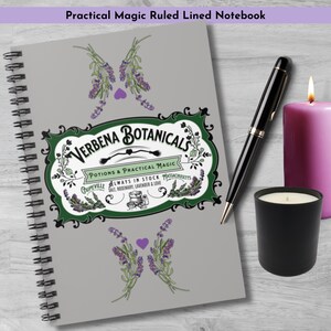 May include: A gray spiral-bound notebook with the text "Practical Magic Ruled Lined Notebook." The cover features a green and white design with the words "Verbena Botanicals" and illustrations of lavender. A black pen, a lit candle, and a black candle holder are next to the notebook.