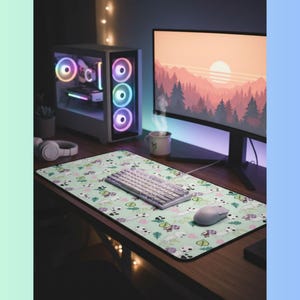 May include: A gaming setup featuring a desktop computer with colorful LED lights, a monitor displaying a sunset scene, and a patterned mousepad. A white keyboard and mouse are on the mousepad. A mug with a cat design is on the desk.