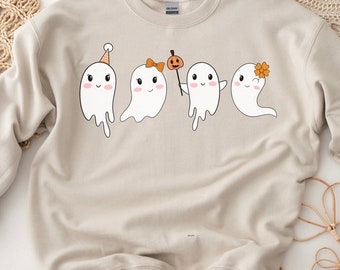 Könnte beinhalten: Ein beiger Pullover mit einem Motiv von vier niedlichen Geistern. Die Geister sind weiß und haben schwarze Augen und Münder. Ein Geist trägt eine Partymütze, einer hat eine Schleife, einer hält einen Stock mit einem Kürbis darauf und einer hat eine Blume auf dem Kopf.