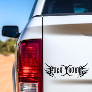 May include: Black vinyl decal with the words "FUCK TRUMP" in a stylized, gothic font. The decal is affixed to the white rear of a vehicle, near the taillight.