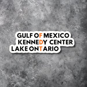 May include: A white die-cut sticker featuring the black text GULF OF MEXICO, KENNEDY CENTER, and LAKE ONTARIO, with the orange letters F, D, and T stacked vertically in the center to form the word FDT across the three lines of text.