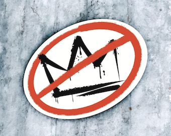 May include: An oval sticker featuring a black graffiti-style crown graphic centered on a white background, crossed out by a bold, textured orange diagonal line. The design has a distressed, spray-painted aesthetic with visible paint drips.