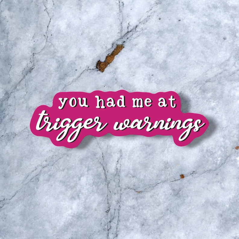 May include: Pink sticker with white lettering on a gray marble background. The sticker says "You had me at trigger warnings."