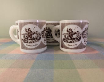 May include: Three white mugs with a brown and white illustration of a hunting scene, with the text "Currier & Ives". The mugs have white handles and are arranged on a plaid surface.