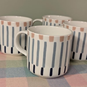 May include: Four white ceramic mugs with a blue and pink striped pattern. The mugs have a handle on the right side.